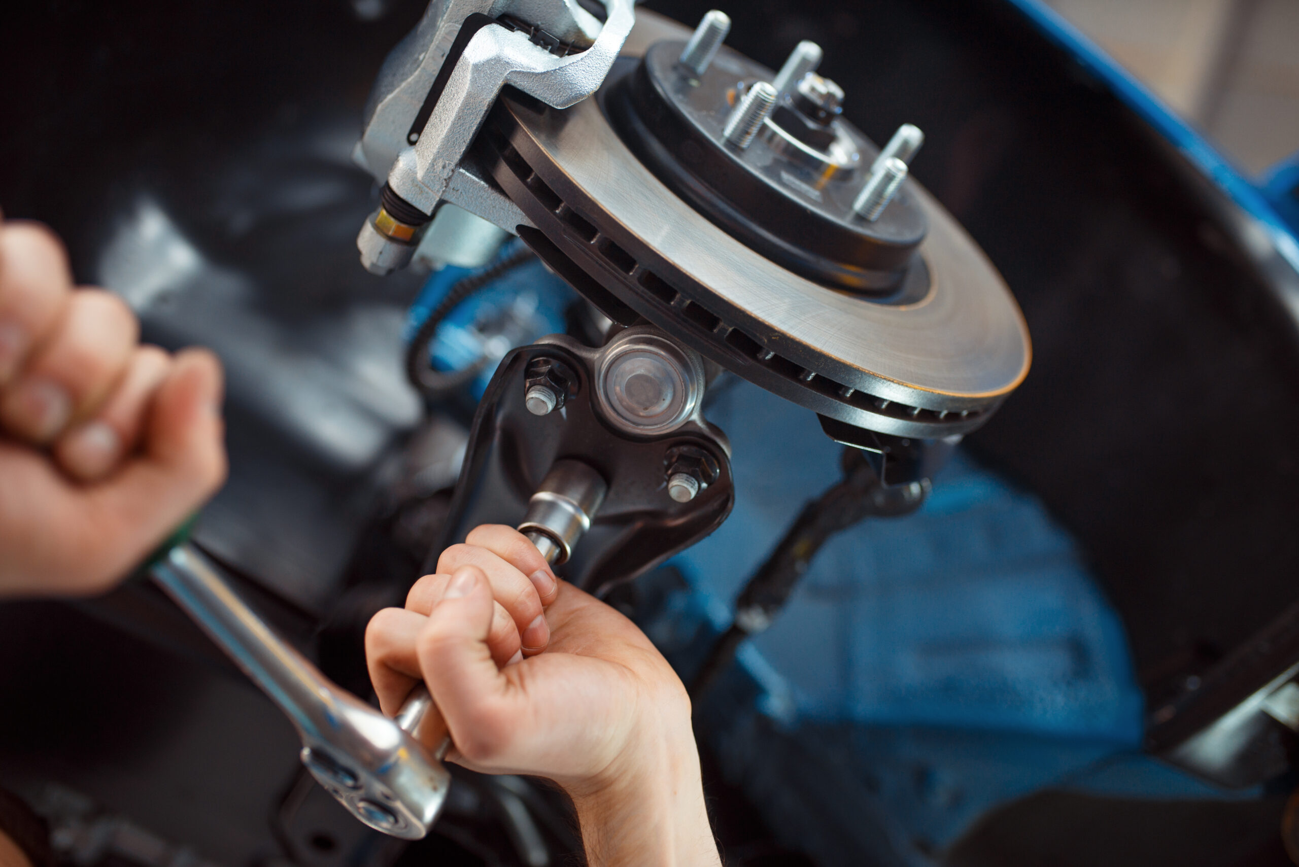 Worker in uniform repairing vehicle on lift, car service station. Automobile checking and inspection.